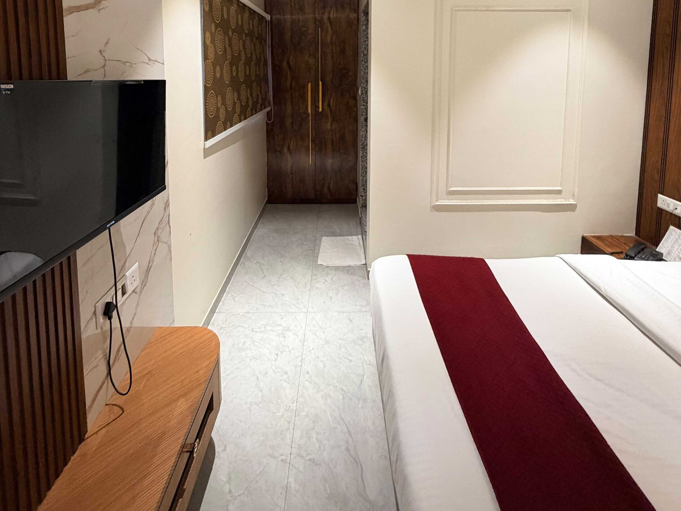 A hotel room with a bed, a TV mounted on the wall, a wooden nightstand, and a door leading to a bathroom.