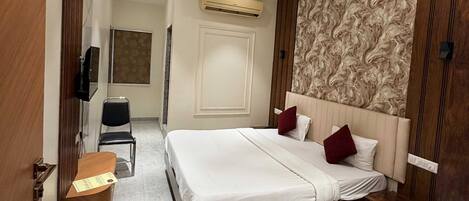 A hotel room with a bed, a desk, a chair, an air conditioning unit, and a television.