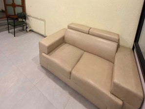 Un sofá de cuero color beige en una habitación con piso de baldosas y un radiador.