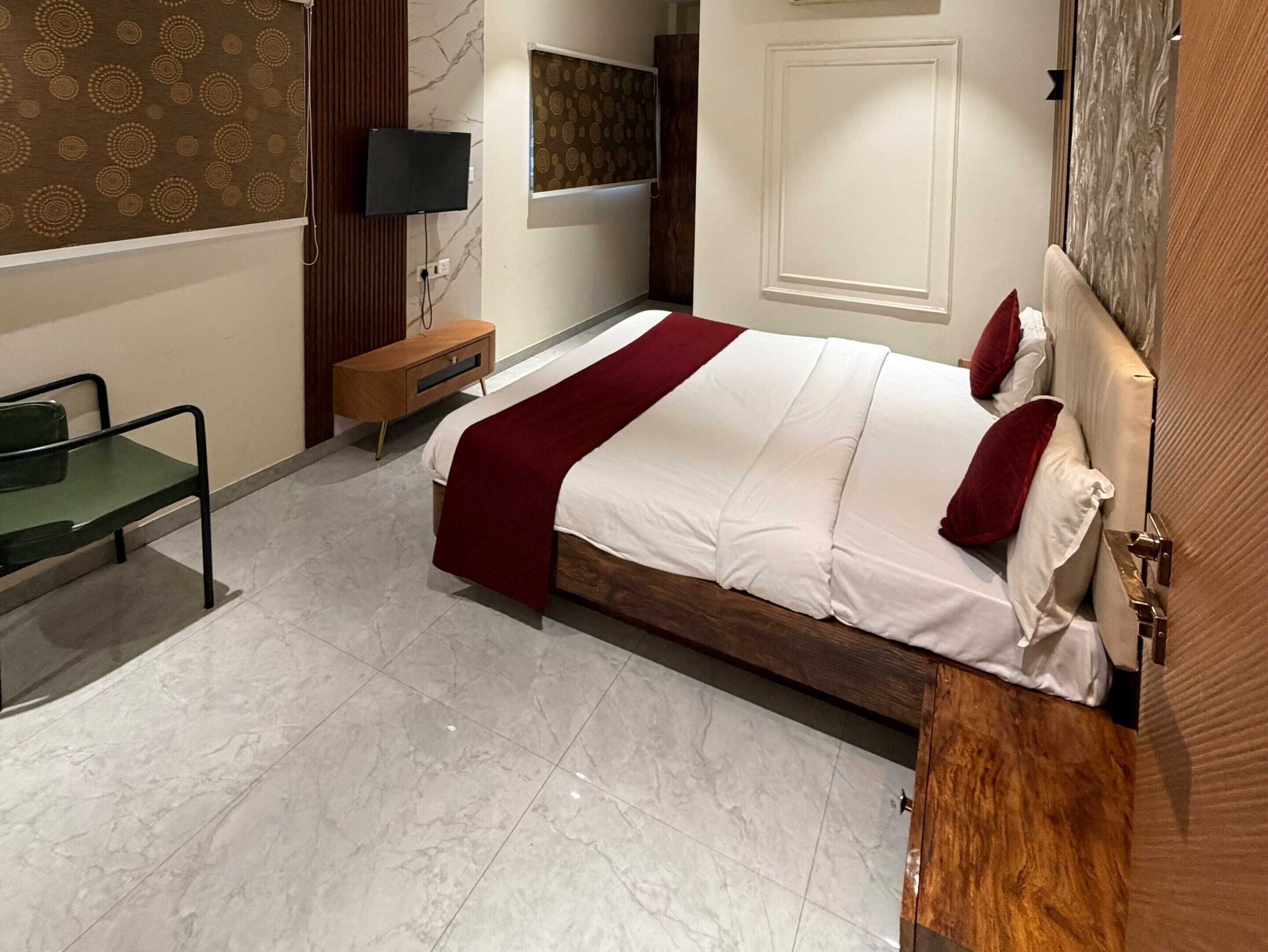 A hotel room with a bed, a TV, a wooden nightstand, a chair, and a patterned wall.
