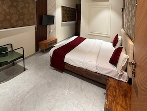 Una habitación de hotel con una cama, un televisor, una mesita de noche de madera, una silla y un papel tapiz estampado.