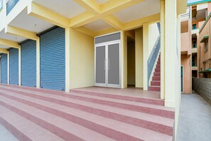 Eine Gebäudefassade mit geschlossenen Rollläden, eine Treppe, die zu einem Eingang führt, und eine sichtbare Wendeltreppe zu einer oberen Etage.
