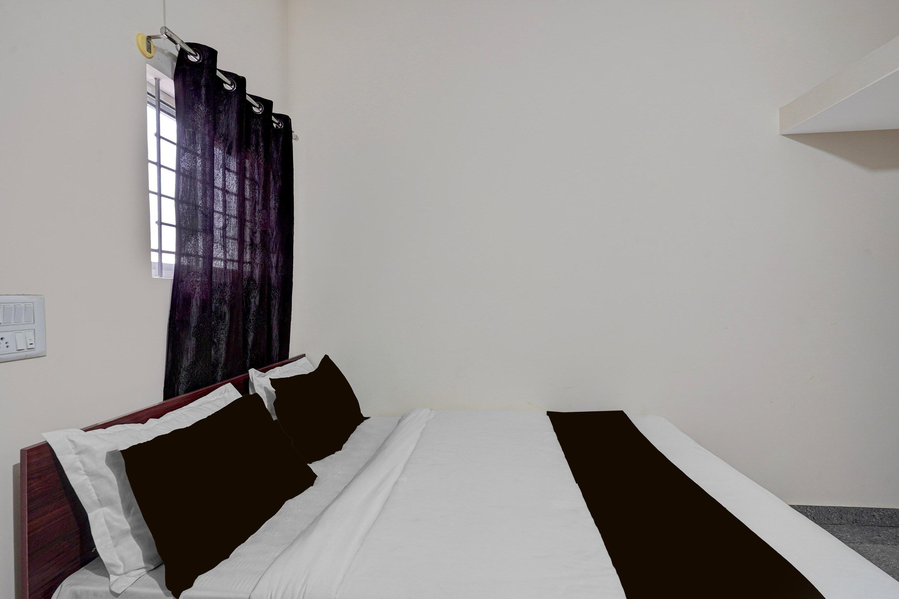 A single bed with a white and black bedspread, a headboard, and a window with a curtain.