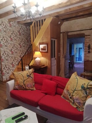 Ein gemütliches Wohnzimmer mit einem roten Sofa, gemusterten Kissen, einer Holztreppe und einer Chandelier.