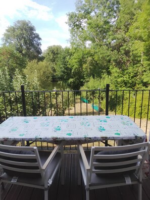 A table with a patterned tablecloth, two white chairs, and a metal railing. - Charming Riverside Gite in the Brenne National Park close to amenities. (Belabre)