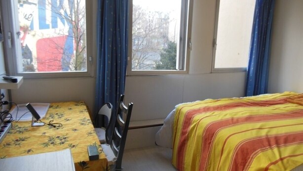 Een slaapkamer met een bed, een bureau met een computer en een raam met gordijnen.