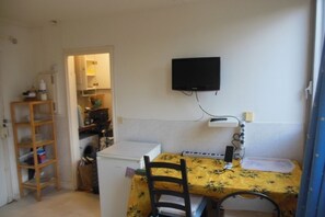 A small kitchen with a table, chairs, a refrigerator, a TV mounted on the wall, and a wooden shelf. - STUDIO APARTMENT IN CENTRAL PARIS (Paris)