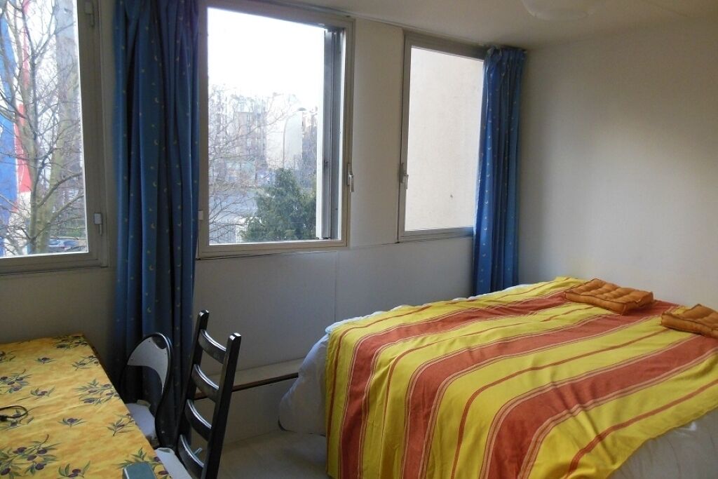 Une pièce comprenant un lit, une chaise, une table et deux fenêtres avec des rideaux.
