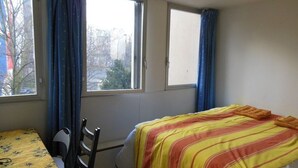 Een kamer met een bed, een stoel, een tafel en twee ramen voorzien van gordijnen.