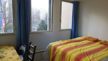 Una stanza con un letto, una sedia, un tavolo e due finestre con tende.