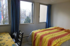 A room with a bed, a chair, a table, and two windows with curtains. - STUDIO APARTMENT IN CENTRAL PARIS (Paris)