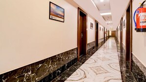 Un corridoio d'hotel con pavimento in marmo, porte in legno e un estintore sulla parete.