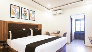 Una camera d'albergo con un letto grande, un comodino con un telefono, una macchina per caffè e una sedia. Si apre una porta su un balcone con vista.