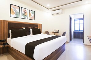 Ein Hotelzimmer mit einem großen Bett, einem Nachttisch mit Telefon, einer Kaffeemaschine und einem Sessel. Eine Tür führt zu einem Balkon mit Blick.