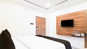 Una camera d'albergo con un letto, una televisione montata su un pannello di legno, una porta e un piccolo ripiano con degli oggetti.