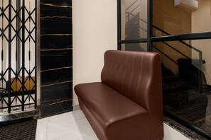 Eine braune Lederbank in einer Empfangshalle mit einer Wand in Schwarz und Gold sowie einer Glastür zu einer Treppe.
