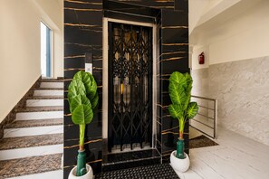 A modern interior with a black and gold marble staircase, a black elevator door, and two large potted plants. - Deluxe Lavish Stays (Hyderabad)