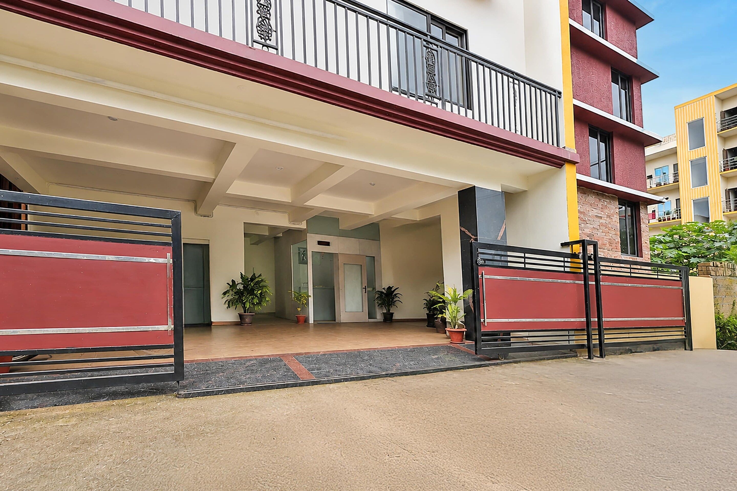 A building entrance with a gated driveway, potted plants, and a clear sky.