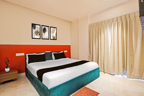 A hotel room with a bed, a nightstand, a vase of flowers, and a window with curtains.
