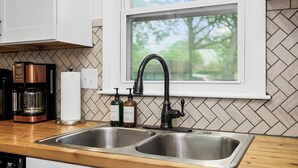Cocina con un lavamanos doble, cafetera y dos dispensadores de jabón.