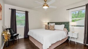 Un dormitorio con cama, mesita de noche, silla, ventana y ventilador de techo.