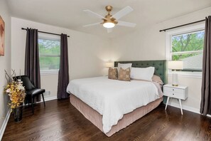 A bedroom with a bed, a nightstand, a chair, a window, and a ceiling fan. - Modern 3BR, Sleeps 9, Mins to Arrowhead & KC (Raytown)