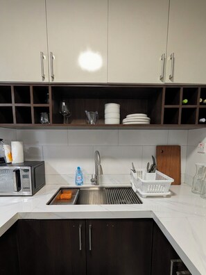 A kitchen with a stainless steel sink, a microwave, and a cutting board. - Central Retreat (Kingston)