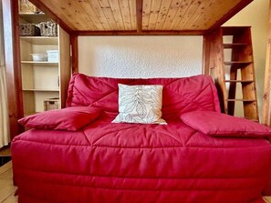 A red sofa with a patterned pillow in a room with wooden beams on the ceiling and shelves with baskets. - Ground floor, terrace, parking, 20m², Serre Chevalier (La Salle-les-Alpes)