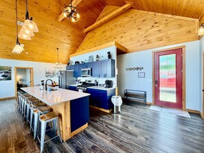 Una cocina moderna con una isla central, taburetes de bar y techo de madera.