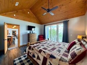 Ein Schlafzimmer mit einem großen Bett, einem Deckenventilator, einer hölzernen Kommode und Blick ins Freie durch eine Schiebetür.