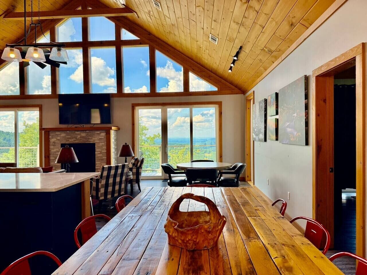 A spacious dining area with a long wooden table, red chairs, and a view of the outdoors through large windows.