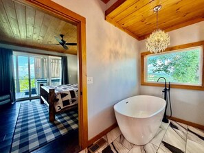 A bathroom with a freestanding bathtub, a window with a view of greenery, and a checkered floor. - Million-Dollar Views 4BR Hot Tub /Game Room/ Pool (Gatlinburg)