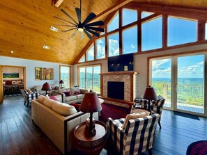 A spacious living room with a fireplace, large windows, and a high ceiling fan. - Million-Dollar Views 4BR Hot Tub /Game Room/ Pool (Gatlinburg)