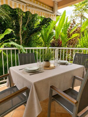 An outdoor dining area with a table set for four, surrounded by chairs, with a view of lush greenery. - Apartment with a terrace, 150 meters from the ocean (Les Trois-Îlets)