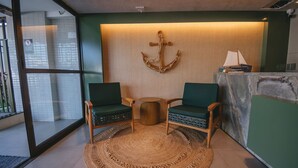 A room with two green chairs, a woven rug, a wooden table, and a wall-mounted anchor decoration. - Luxury studio apartment 3 minutes from the natural pools (Ipojuca)