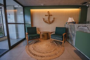 Ein Zimmer mit zwei grünen Stühlen, einem gewebten Teppich, einem Holztisch und einer Wanddekoration als Anker.