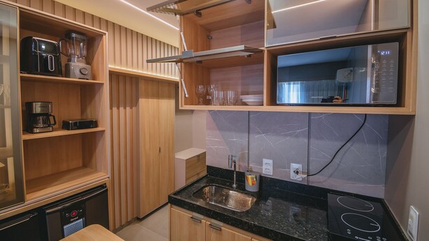 A compact kitchen with built-in appliances, a countertop sink, and wooden cabinetry. - Luxury studio apartment 3 minutes from the natural pools (Ipojuca)