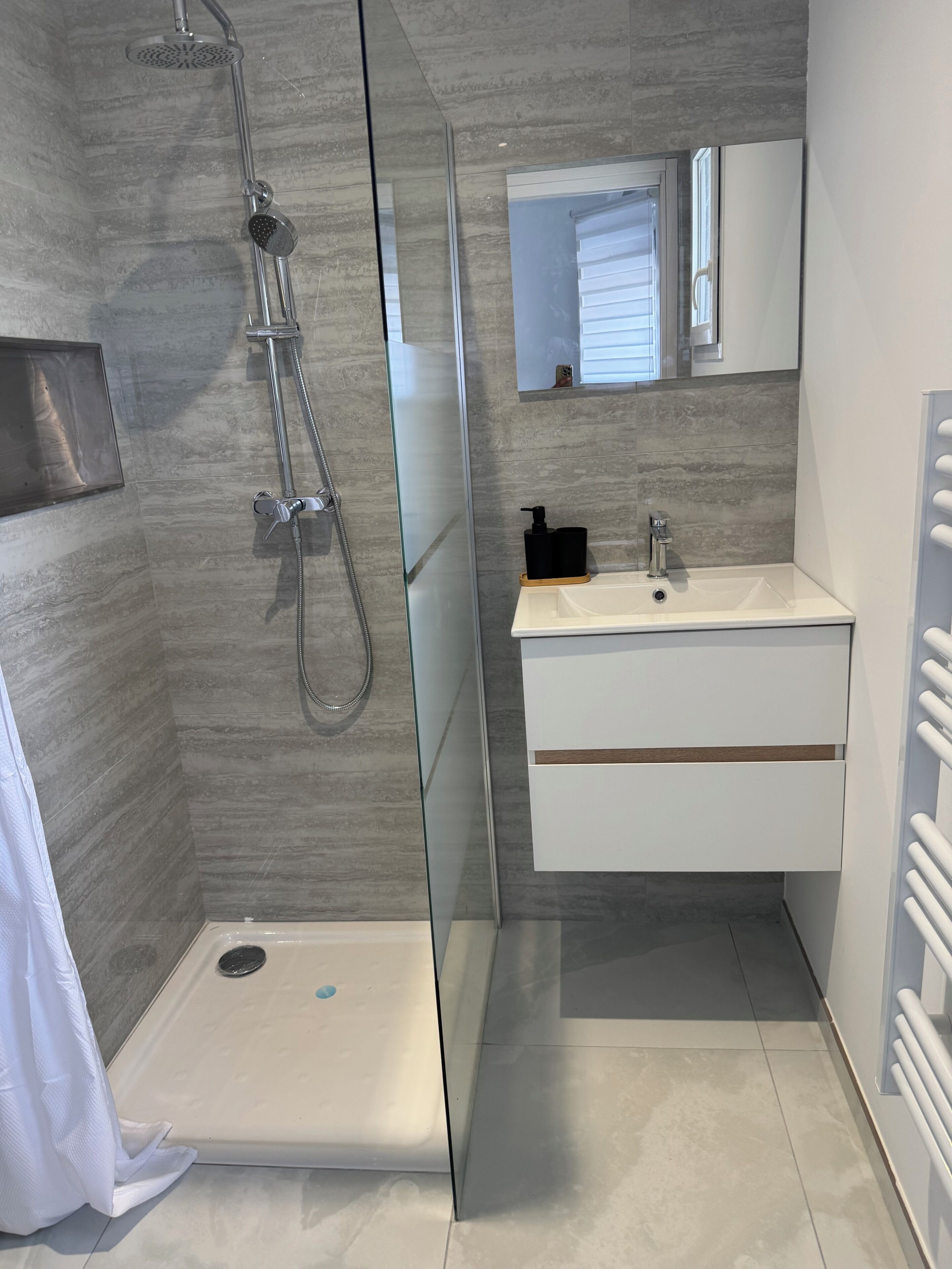 Een moderne badkamer met een glazen douchecabine, een wit wastafeltje met een spiegel erboven en een handdoekrek.