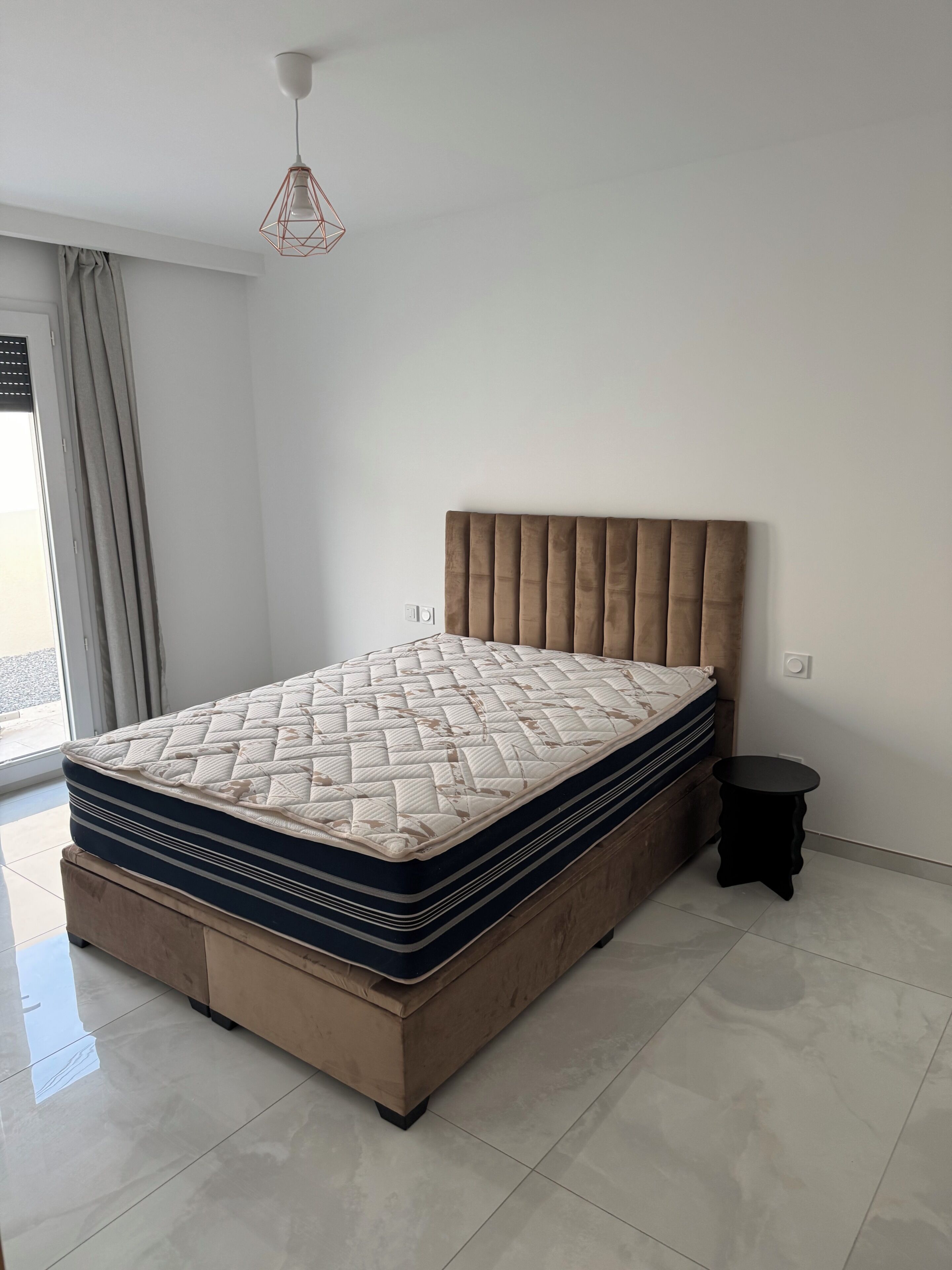 A bedroom with a large bed, a bedside table, and a hanging light fixture.