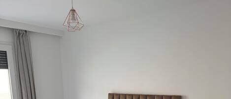 A bedroom with a large bed, a bedside table, and a hanging light fixture.