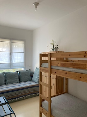 A bunk bed with a potted plant on top, a sofa with striped cushions, and a window with blinds. - The Oleander (Venezia)