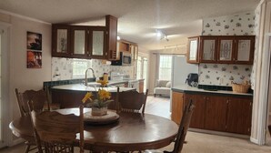 A kitchen with wooden cabinets, a dining table with chairs, and a clock on the wall. - Cozy Lakehouse Gem In the Woods (Hephzibah)