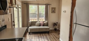 A compact living space with a kitchenette, a sofa, a potted plant, and a window with curtains.