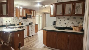 A kitchen with wooden cabinets, a white stove, and a microwave. - Cozy Lakehouse Gem In the Woods (Hephzibah)