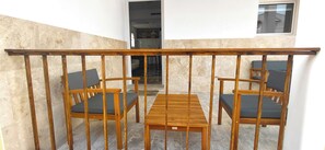 Ein Balkon mit Holztisch und vier Stühlen, Blick ins Innere durch eine offene Tür und ein Fenster auf der rechten Seite.