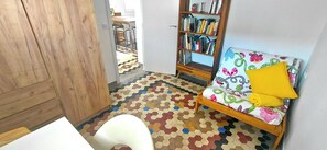 Ein Zimmer mit Holztür, weißem Stuhl, einer Couch mit Blumenmuster und einem Bücherregal, sowie einem fußbodenmuster.