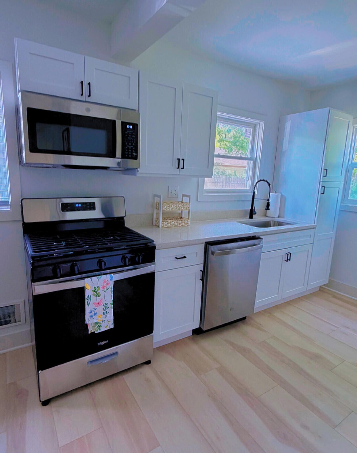 A modern kitchen with stainless steel appliances, white cabinetry, and a wooden floor.