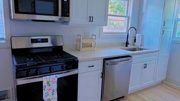 A modern kitchen with stainless steel appliances, white cabinetry, and a wooden floor.
