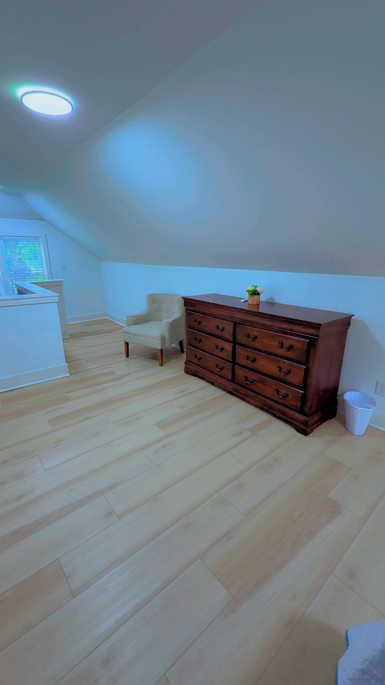 A room with a wooden floor, a dresser with drawers, a chair, and a desk with a computer monitor.