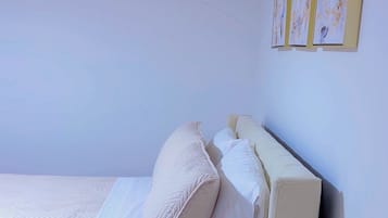 Un lit simple avec un cadre en bois et une literie blanche, dans une pièce aux murs de couleur claire et au plancher en bois.